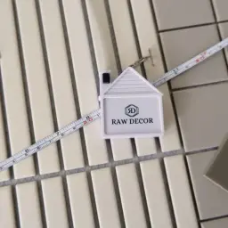 Miarka w kształcie domu i linijka pomagają ustalić, jak rozmierzyć płytki na podłodze.
