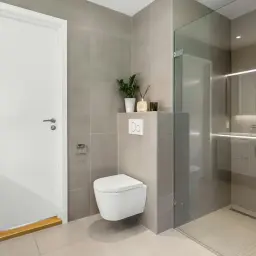 Nowoczesna łazienka z białym WC i prysznicem. Dowiedz się, jak odnowić łazienkę, nie wymieniając kafelków, dodając nowe akcesoria i oświetlenie.