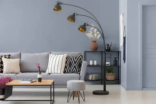 Nowoczesny salon z szarą ścianą, szarą kanapą, stolikiem kawowym i łukową lampą.