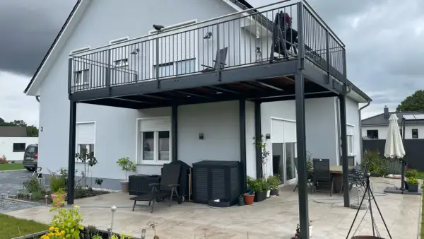 Nowoczesny balkon dostawny cena – stalowa konstrukcja z balustradą, meble ogrodowe i rośliny na tarasie.