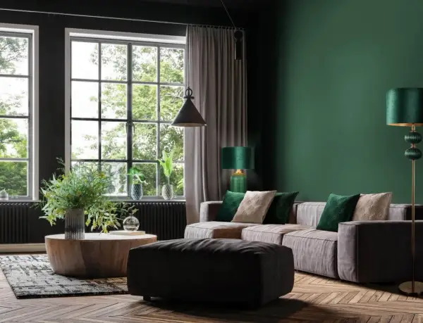 Elegancki salon z kanapą, stolikiem i pufą. Ściana w kolorze butelkowa zieleń ze złotem dodaje luksusu.
